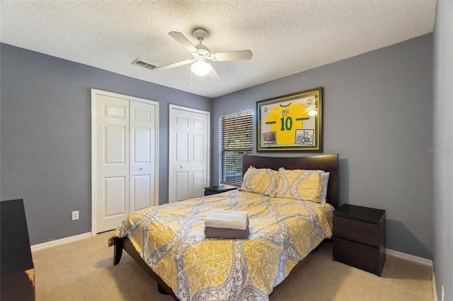 carpeted bedroom with multiple closets, ceiling fan, and a textured ceiling