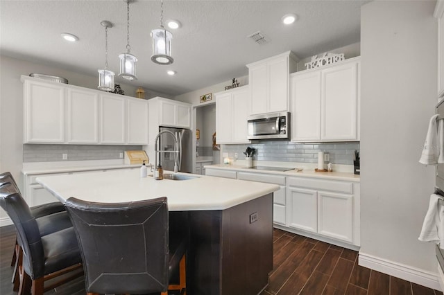 kitchen featuring white cabinetry, hanging light fixtures, stainless steel appliances, and a center island with sink