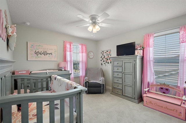 bedroom with a crib, ceiling fan, light colored carpet, and a textured ceiling