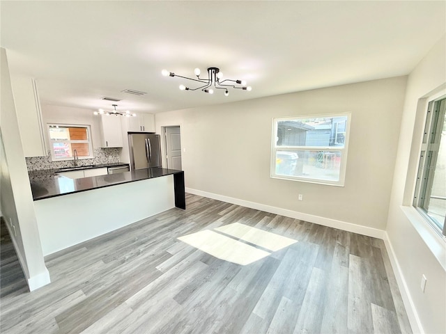 kitchen featuring decorative light fixtures, a chandelier, stainless steel fridge, a healthy amount of sunlight, and white cabinets