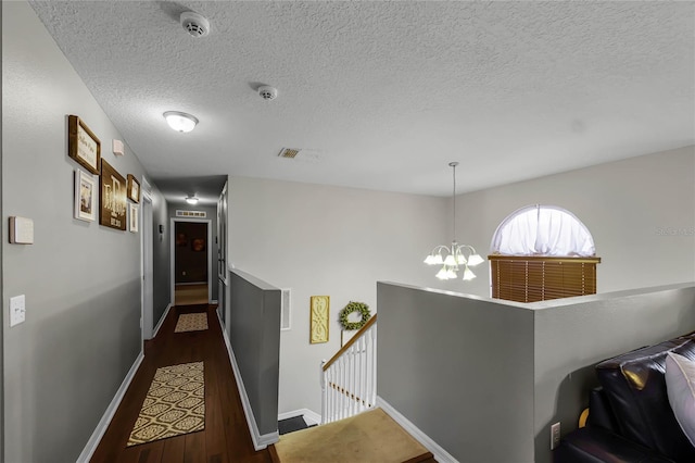 corridor with baseboards, visible vents, dark wood-style flooring, an upstairs landing, and a notable chandelier