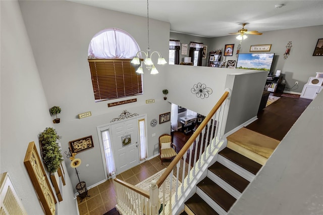 foyer featuring ceiling fan with notable chandelier, a high ceiling, stairway, and baseboards