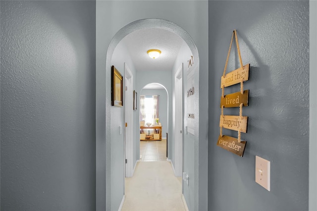 corridor featuring light carpet, arched walkways, a textured ceiling, and a textured wall