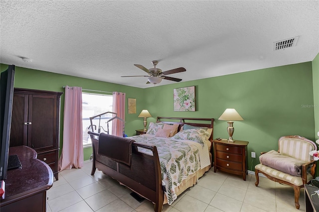 bedroom featuring a textured ceiling, light tile patterned floors, visible vents, baseboards, and a ceiling fan