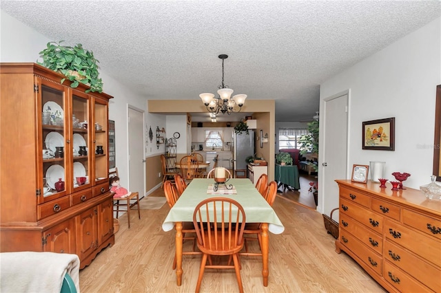 dining area featuring an inviting chandelier, a textured ceiling, and light wood-type flooring