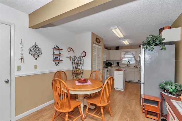 dining space with sink, light hardwood / wood-style flooring, and a textured ceiling