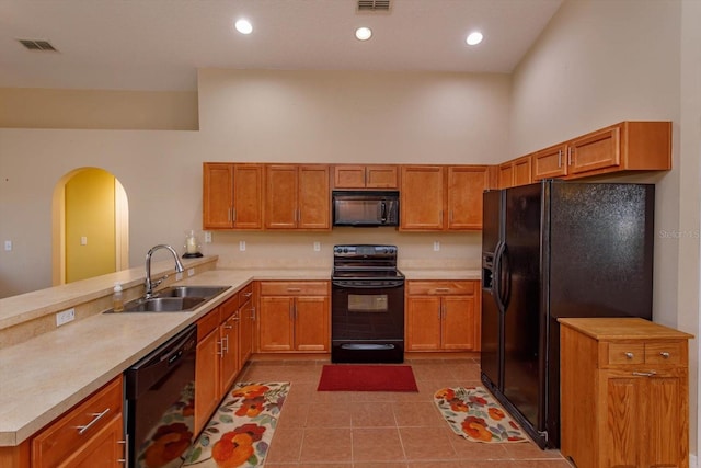 kitchen featuring sink, light tile patterned floors, a towering ceiling, black appliances, and kitchen peninsula