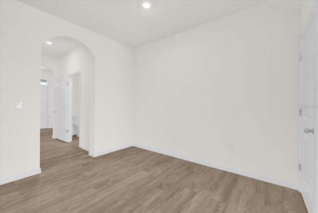 spare room with light wood-style flooring, arched walkways, and baseboards