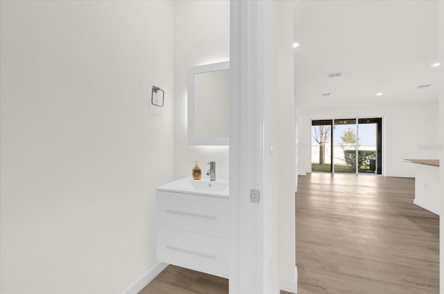 hall with visible vents, baseboards, light wood-style flooring, a sink, and recessed lighting