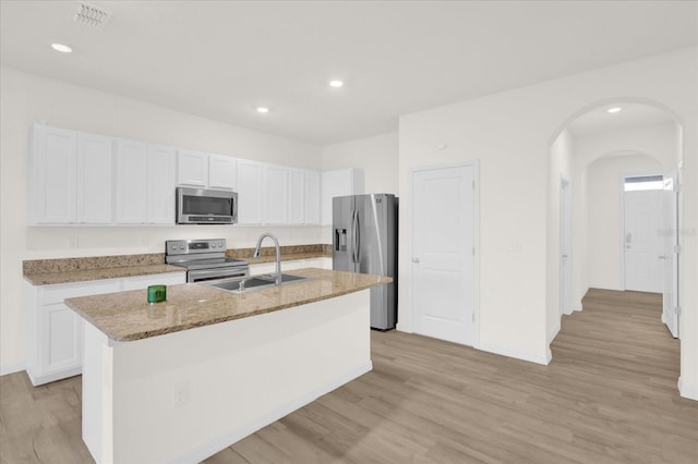 kitchen with arched walkways, a sink, white cabinetry, appliances with stainless steel finishes, and an island with sink