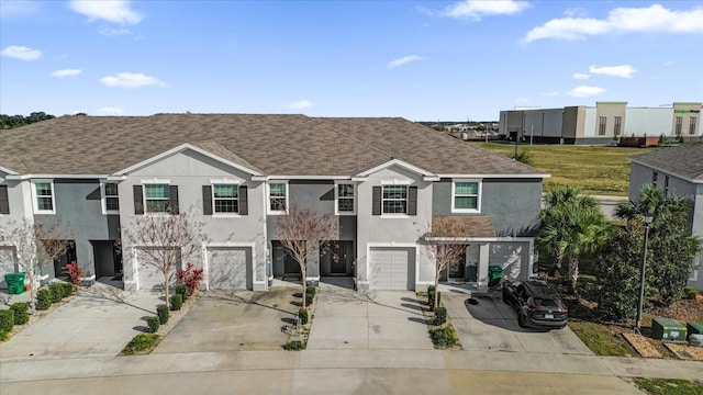 multi unit property with a garage, driveway, roof with shingles, and stucco siding