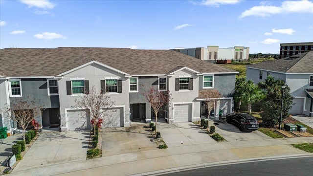 multi unit property with a garage, driveway, a shingled roof, and stucco siding