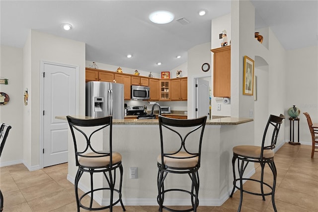 kitchen featuring appliances with stainless steel finishes, a breakfast bar, lofted ceiling, light stone counters, and kitchen peninsula