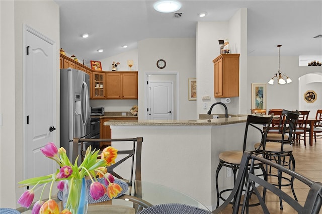 kitchen with pendant lighting, lofted ceiling, stainless steel fridge, light stone counters, and kitchen peninsula