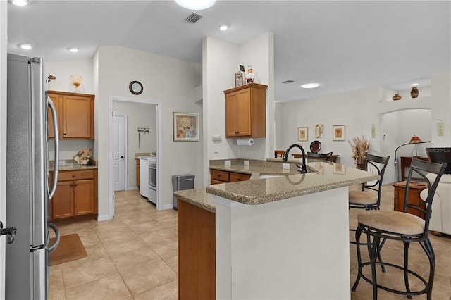 kitchen with sink, a breakfast bar area, stainless steel fridge, kitchen peninsula, and stone counters