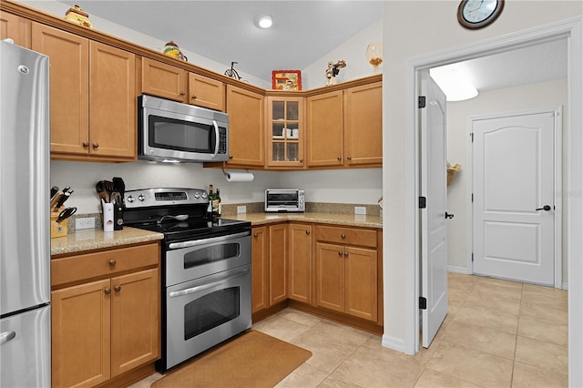 kitchen featuring light stone counters, stainless steel appliances, vaulted ceiling, and light tile patterned floors