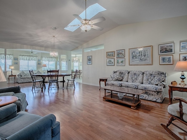 living room with wood-type flooring, ceiling fan with notable chandelier, and vaulted ceiling with skylight