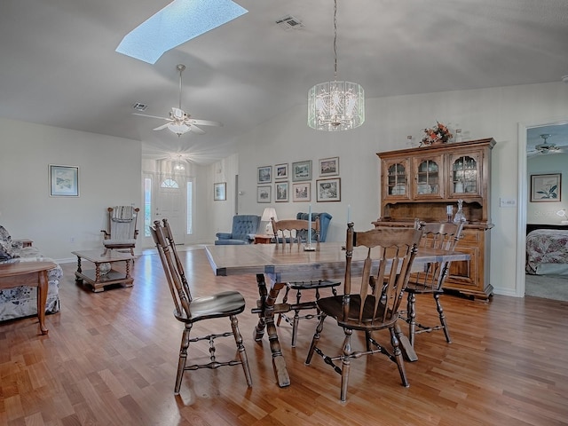 dining room with lofted ceiling with skylight, ceiling fan with notable chandelier, and light hardwood / wood-style flooring