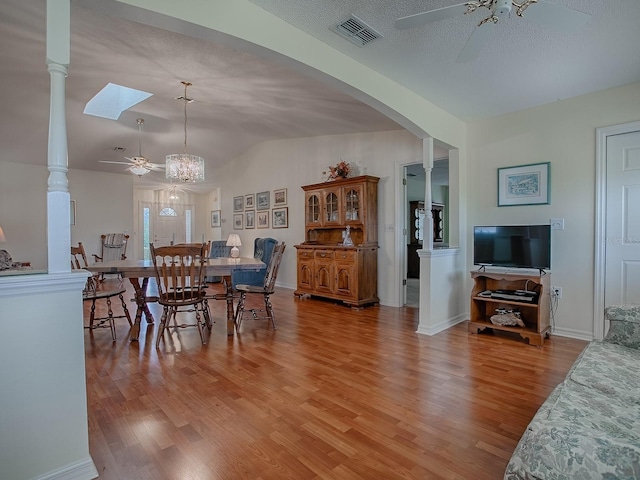 dining area featuring hardwood / wood-style floors, vaulted ceiling with skylight, and ceiling fan with notable chandelier