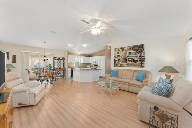 living room with ceiling fan with notable chandelier, vaulted ceiling, a textured ceiling, and light wood-type flooring