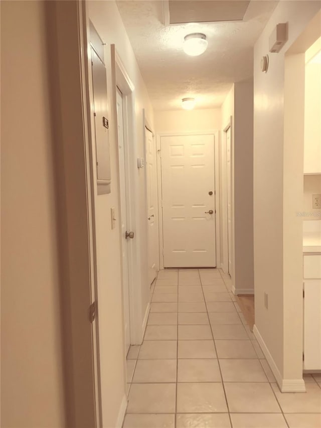 hall with light tile patterned floors, a textured ceiling, and baseboards