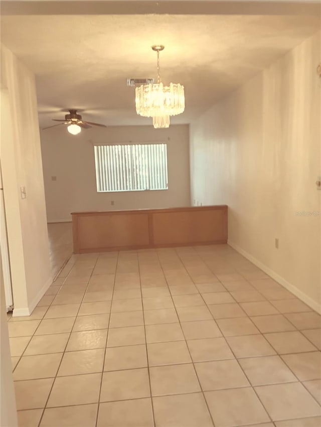 empty room featuring light tile patterned floors, baseboards, visible vents, and ceiling fan with notable chandelier