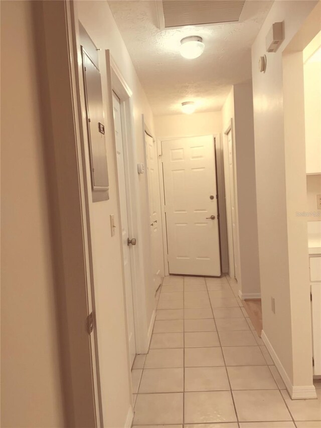 corridor with electric panel, baseboards, a textured ceiling, and light tile patterned flooring