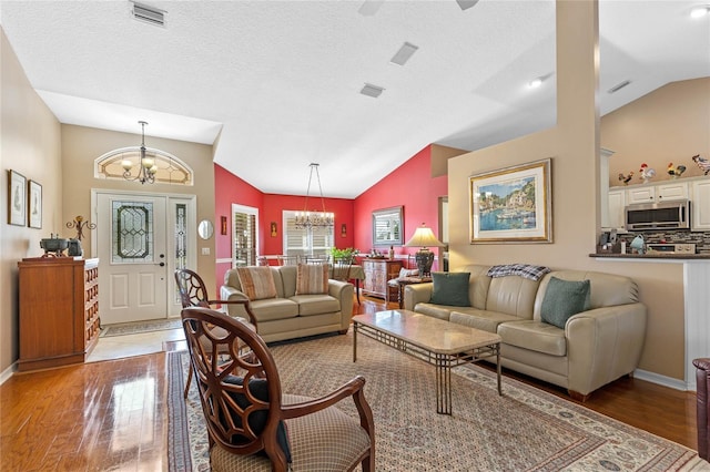 living room featuring vaulted ceiling, hardwood / wood-style floors, a notable chandelier, and a textured ceiling