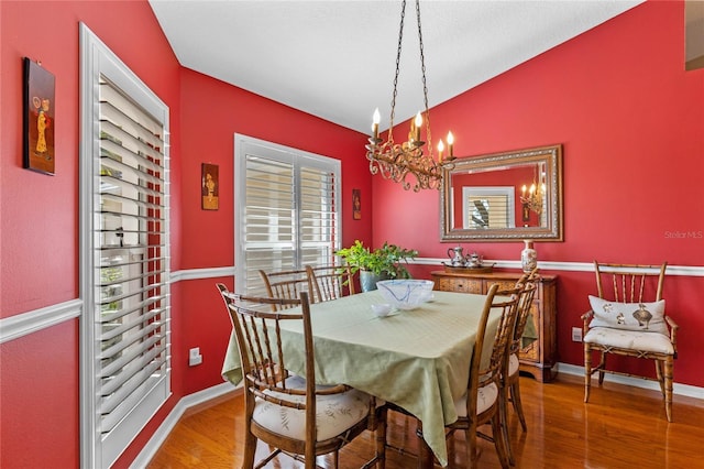 dining space with lofted ceiling, hardwood / wood-style floors, and a notable chandelier