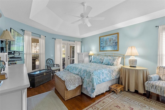 bedroom featuring hardwood / wood-style flooring, ceiling fan, a tray ceiling, access to outside, and french doors