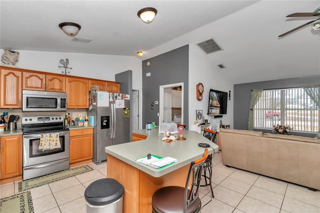 kitchen with vaulted ceiling, light tile patterned flooring, a center island, stainless steel appliances, and a breakfast bar area