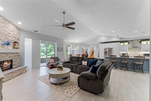 living room with a stone fireplace, vaulted ceiling, and ceiling fan