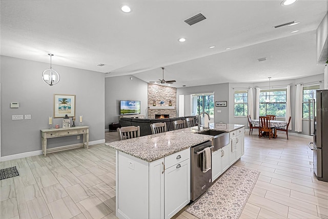 kitchen featuring sink, appliances with stainless steel finishes, a kitchen island with sink, light stone countertops, and white cabinets