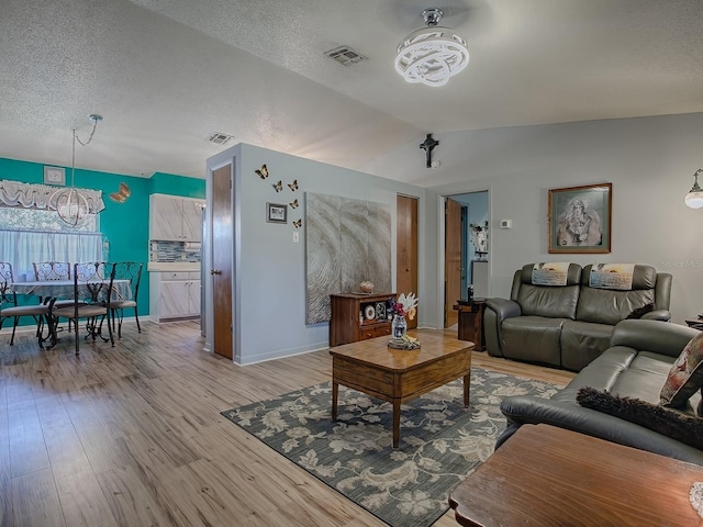 living room featuring vaulted ceiling, light hardwood / wood-style flooring, and a textured ceiling