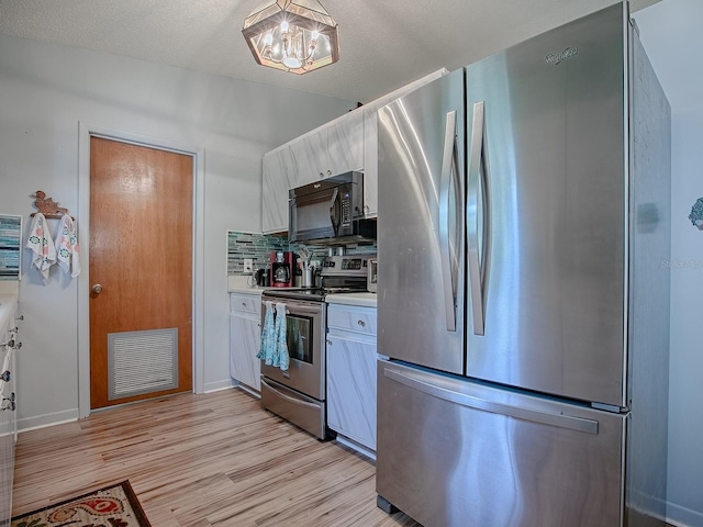 11915 Crk 680, Webster, FL 33597 - kitchen with light hardwood / wood-style flooring, appliances with stainless steel finishes, white cabinets, decorative backsplash, and a chandelier