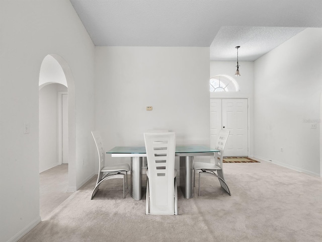 unfurnished dining area with arched walkways, light carpet, a textured ceiling, and baseboards