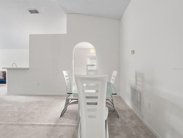 unfurnished dining area featuring light carpet, a textured ceiling, arched walkways, and visible vents