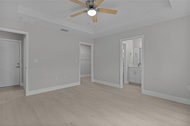 unfurnished bedroom with a raised ceiling, a walk in closet, light wood-type flooring, and a closet