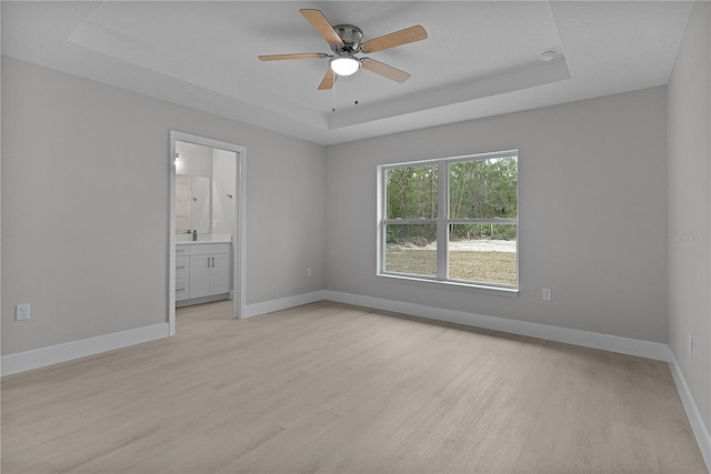 spare room featuring ceiling fan, sink, a tray ceiling, and light hardwood / wood-style floors