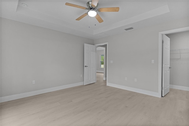 unfurnished bedroom featuring ceiling fan, a raised ceiling, a walk in closet, a closet, and light wood-type flooring