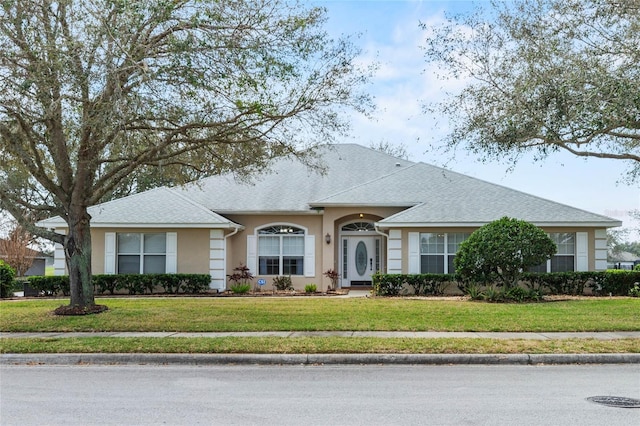 ranch-style home with a shingled roof, a front yard, and stucco siding