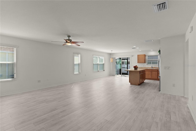 unfurnished living room featuring a sink, visible vents, baseboards, a ceiling fan, and light wood-type flooring