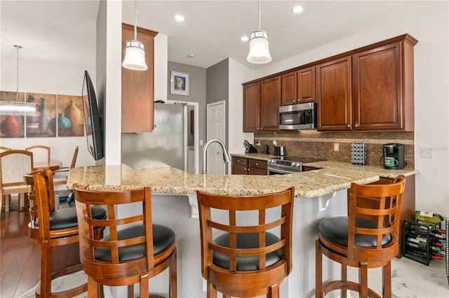 kitchen with appliances with stainless steel finishes, backsplash, decorative light fixtures, and a peninsula