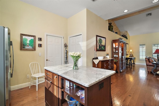 kitchen with lofted ceiling, dark wood-type flooring, stainless steel fridge, light stone countertops, and a kitchen island