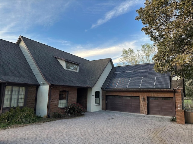 view of front facade featuring an attached garage, decorative driveway, solar panels, and brick siding