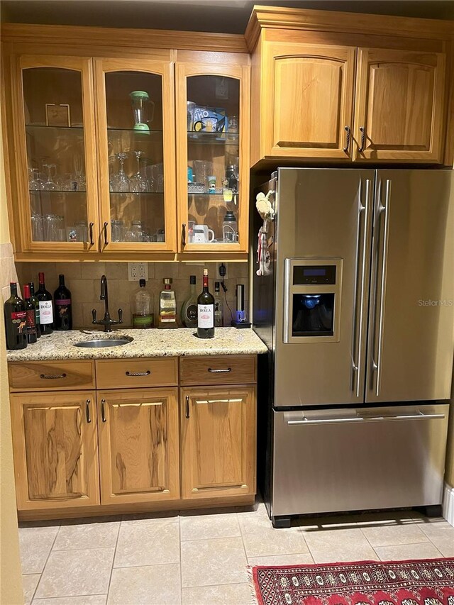 kitchen with glass insert cabinets, light stone countertops, stainless steel refrigerator with ice dispenser, a sink, and light tile patterned flooring