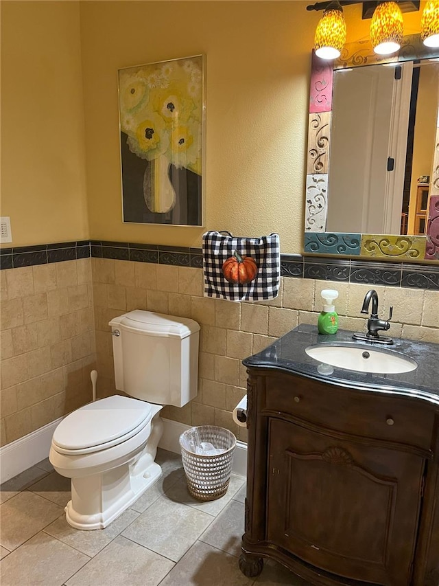 half bathroom with wainscoting, toilet, tile patterned floors, vanity, and tile walls