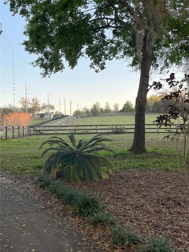 view of property's community with a rural view, fence, and a lawn