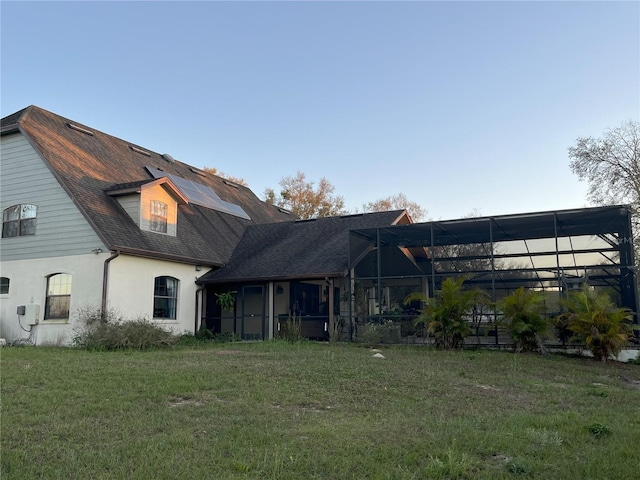 back of property with a shingled roof, a lawn, a lanai, and stucco siding