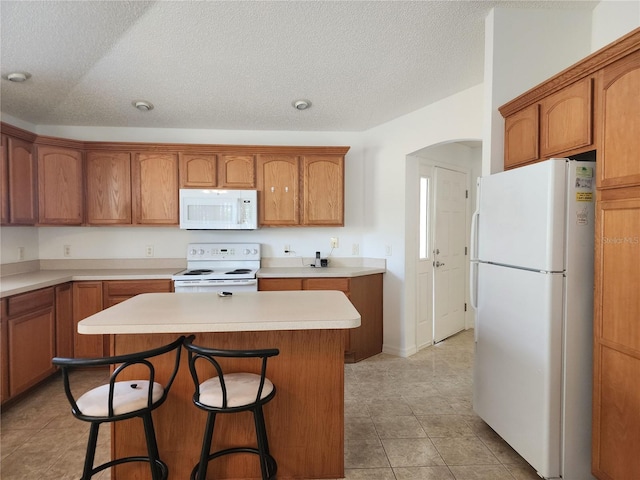 kitchen featuring a textured ceiling, light tile patterned floors, a kitchen breakfast bar, a kitchen island, and white appliances